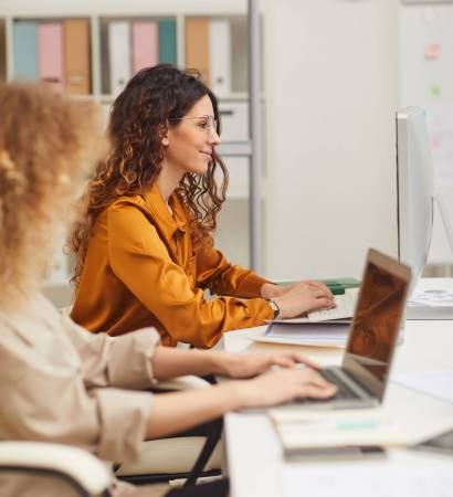 Two Young Businesswomen Working On Computers Women working on computers in modern office vertical side view shot
