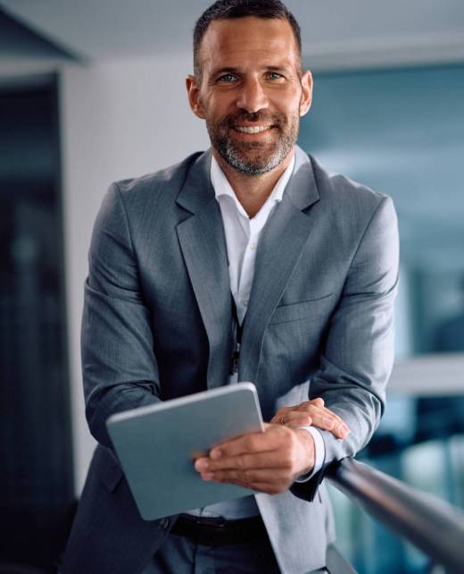 Happy businessman working on touchpad in the office and looking at camera. Happy businessman using digital tablet while working in the office and looking at camera. Copy space.